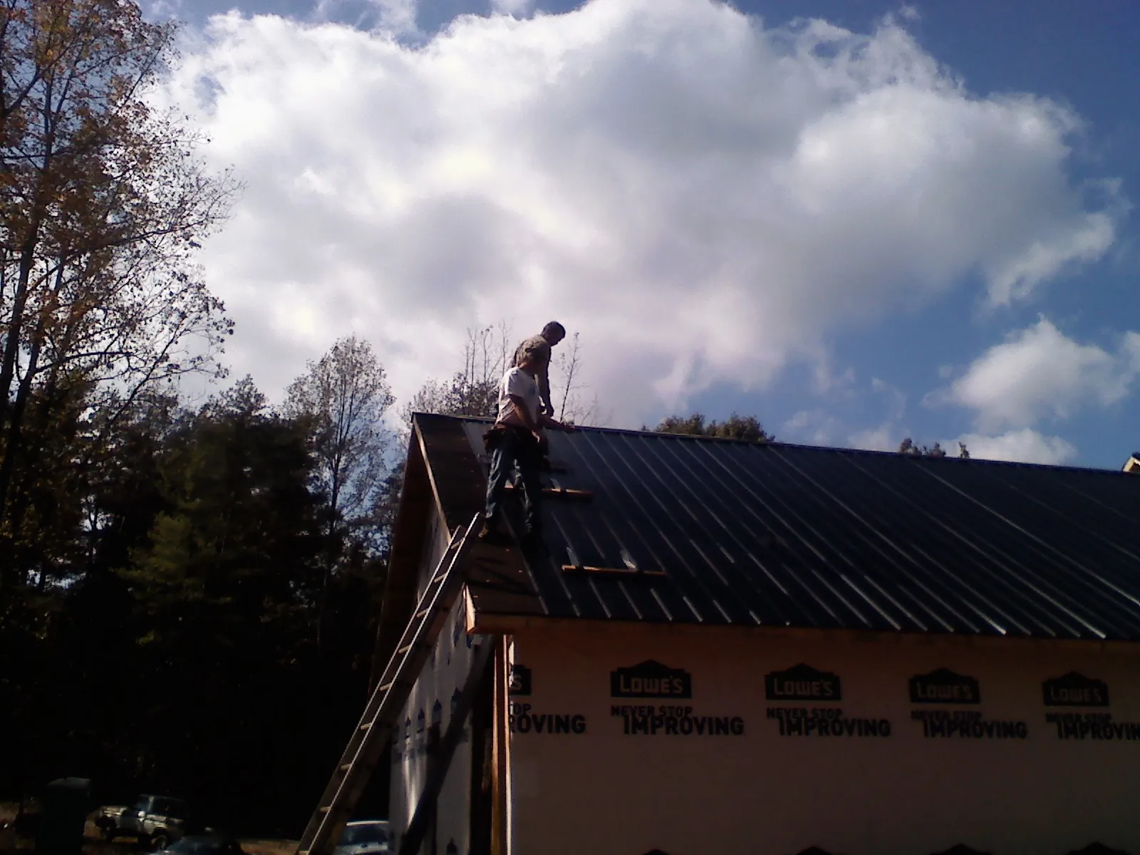 Roofer fastening dark metal panels high against a cloudy sky, from a Roof Inspection job in Lorton