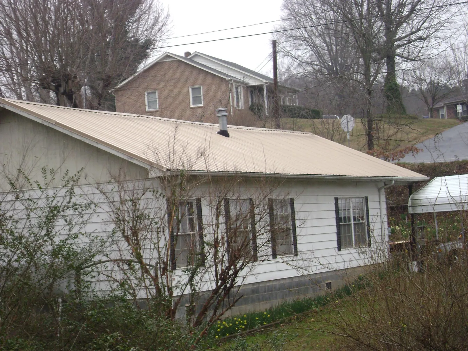 Tan metal roof on a white sided house set into a hillside — Commercial Roofing by Roofing Brothers in Lorton